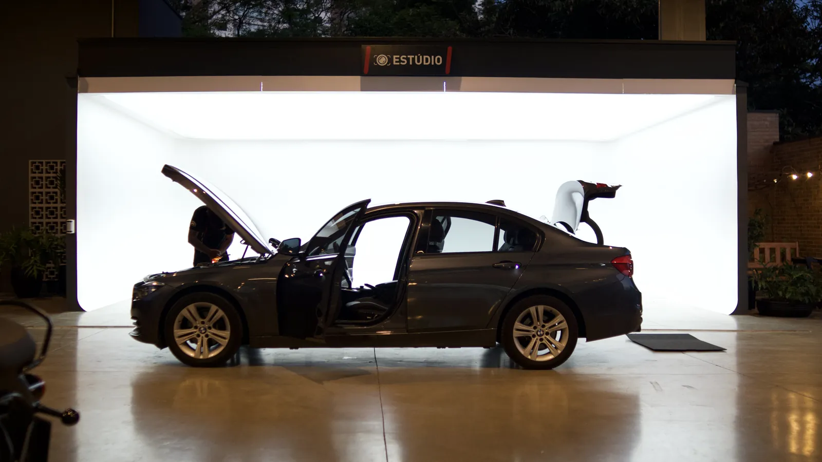 BMW Série 3 com capô, portas e porta-malas abertos sendo preparado em frente ao estúdio de fotos da Kikoautos