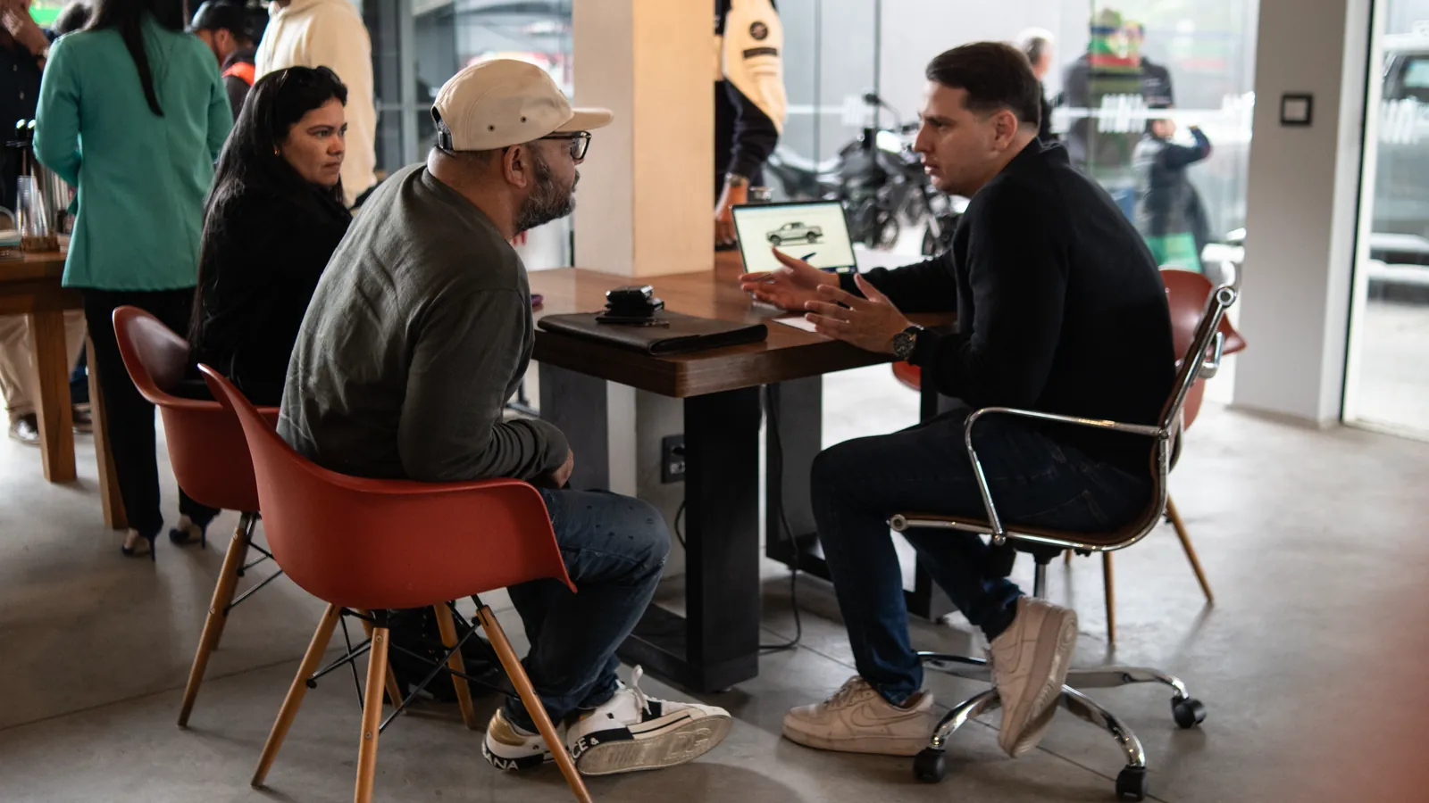 Consultor da Kikoautos conversa com um casal de clientes numa mesa da loja, com um notebook aberto