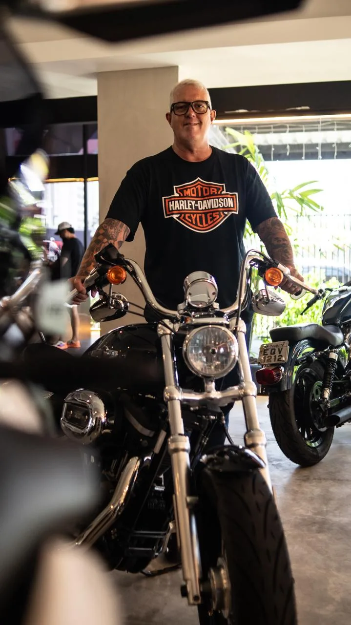 Homem de camiseta Harley-Davidson atrás de uma Sportster preta e cromada, na loja da Kikoautos